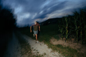 Photo of alpinist Jost Kobusch running on a dirt road next to a corn field.